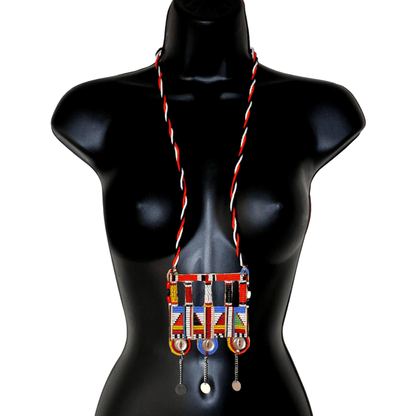 Authentique bijou africain Massai, ce long collier de style sautoir est orné d'un large pendentif à motifs ethniques fait de perles de rocaille multicolores et de boutons nacrés brodés sur un morceau de plastique recyclé ; ils se prolonge de chaînettes décorées de pastilles métalliques.