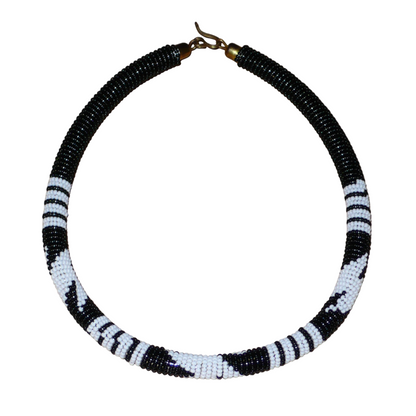 Collier africain tubulaire noir à motifs tribaux zoulous blancs composé de perles de rocaille tissées et enroulées autour d'un tube. Il s'attache avec un crochet.