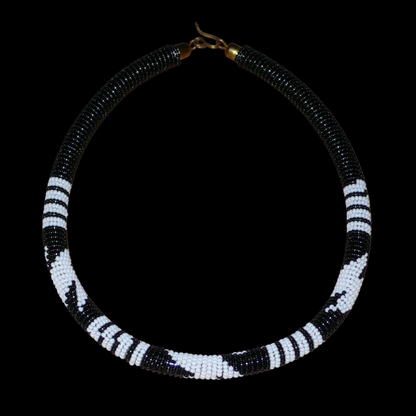 Collier africain tubulaire noir à motifs tribaux zoulous blancs composé de perles de rocaille tissées et enroulées autour d'un tube. Il s'attache avec un crochet.