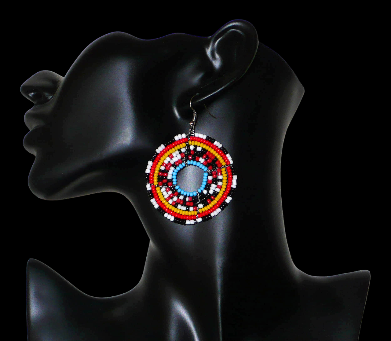 Boucles d'oreilles ethniques composées d'un mélange de perles de rocaille principalement rouges, noires, blanches et bleues montées en cercles. Elles mesurent 6,5 cm de long et 5 cm de large et se portent sur des oreilles percées.