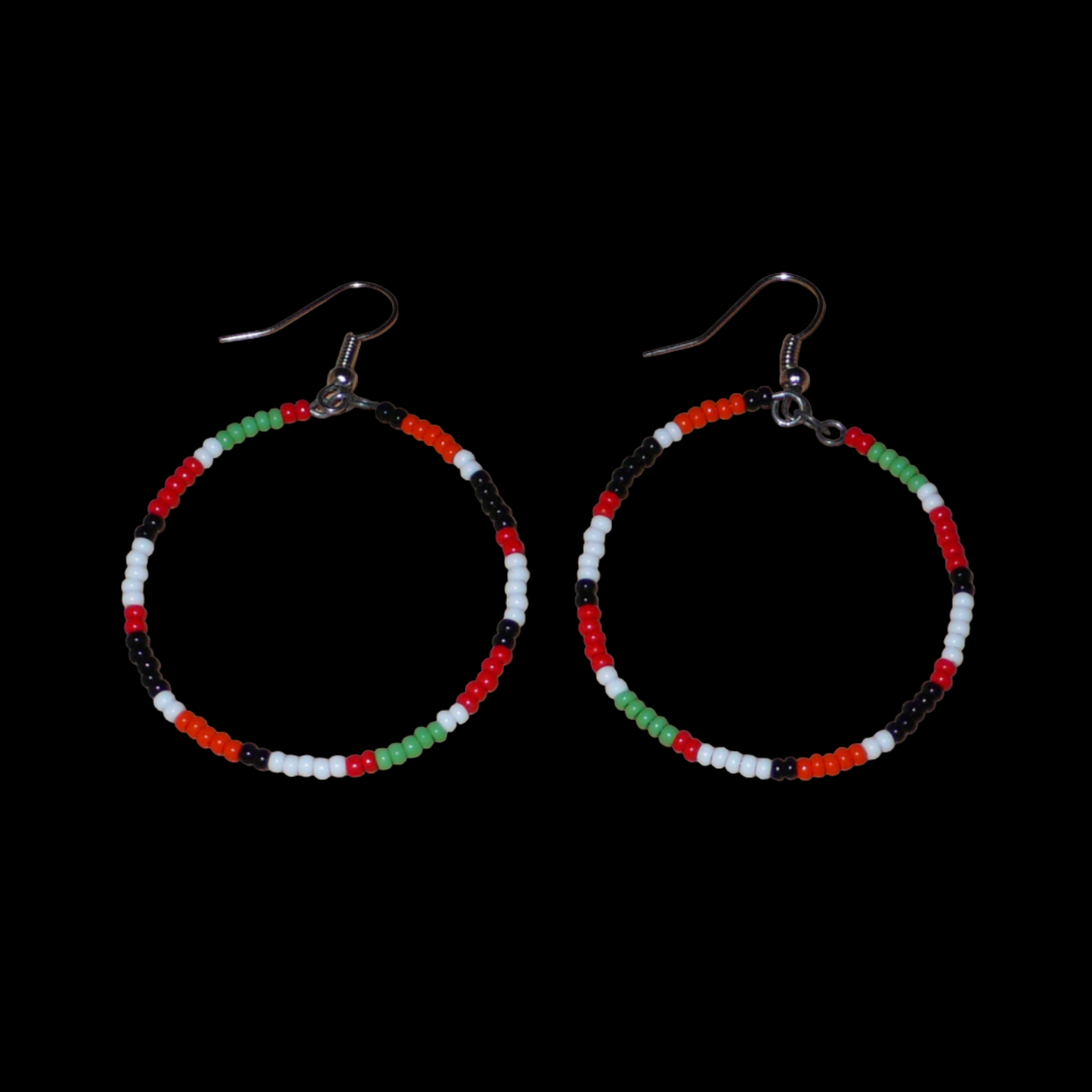Créoles aux couleurs ethniques Massai faites de perles de rocaille rouges, vertes, noires, blanches et orange glissées sur un brin de fils de fer monté en cercle. Elles mesurent 6 cm de long et 4 cm de large, et se portent avec des crochets en acier inoxydable sur des oreilles percées.