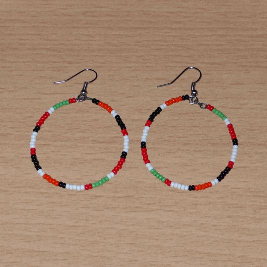 Créoles aux couleurs ethniques Massai faites de perles de rocaille rouges, vertes, noires, blanches et orange glissées sur un brin de fils de fer monté en cercle. Elles mesurent 6 cm de long et 4 cm de large, et se portent avec des crochets en acier inoxydable sur des oreilles percées.
