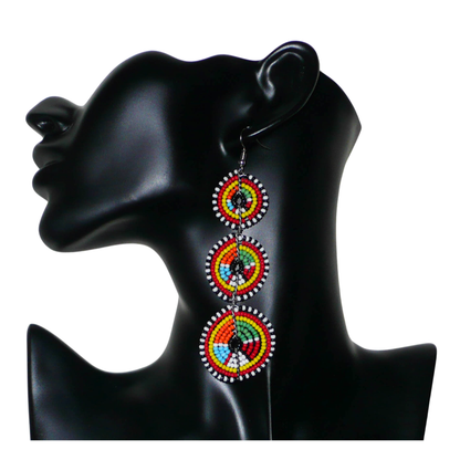 Longues boucles d'oreilles africaines de tradition Massai aux design et couleurs évoquant le style ethnique afro chic des années 70. Elles se composent de perles de rocaille multicolores glissées sur des fils de fer montés en forme de trois cercles superposés. Ces boucles d'oreilles mesurent 10.5 cm de long et 3 cm de large ; elles se portent avec des crochets en acier inoxydable sur des oreilles percées.