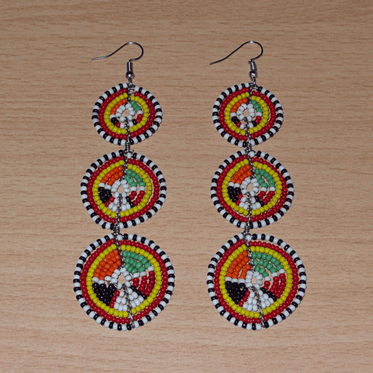 Longues boucles d'oreilles africaines composées de trois cercles superposés en perles de rocaille multicolores. Elles mesurent 11 cm de long et 3 cm de large et se portent avec des crochets en acier inoxydable sur des oreilles percées.