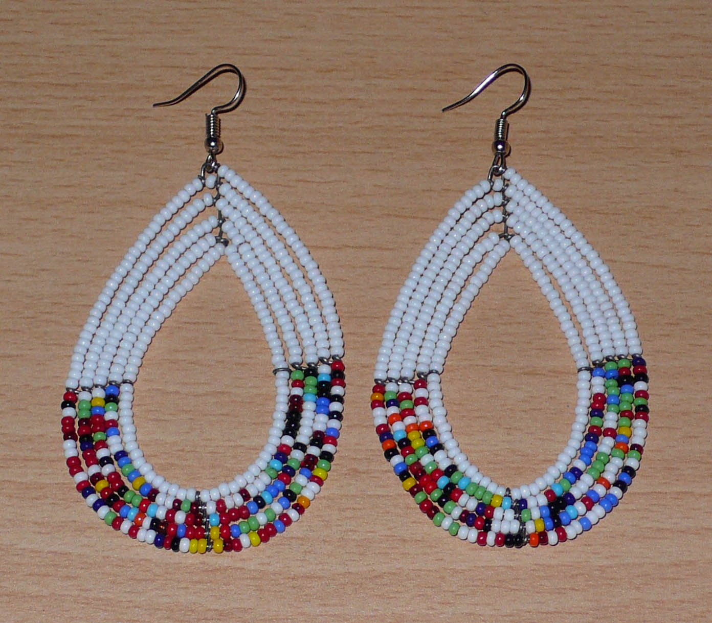 Longues boucles d'oreilles ethniques multi-rangs faites de perles de rocaille blanches et multicolores montées en forme de gouttes. Elles mesurent 9 cm de long et 4.5 cm de large, et se portent sur des oreilles percées.