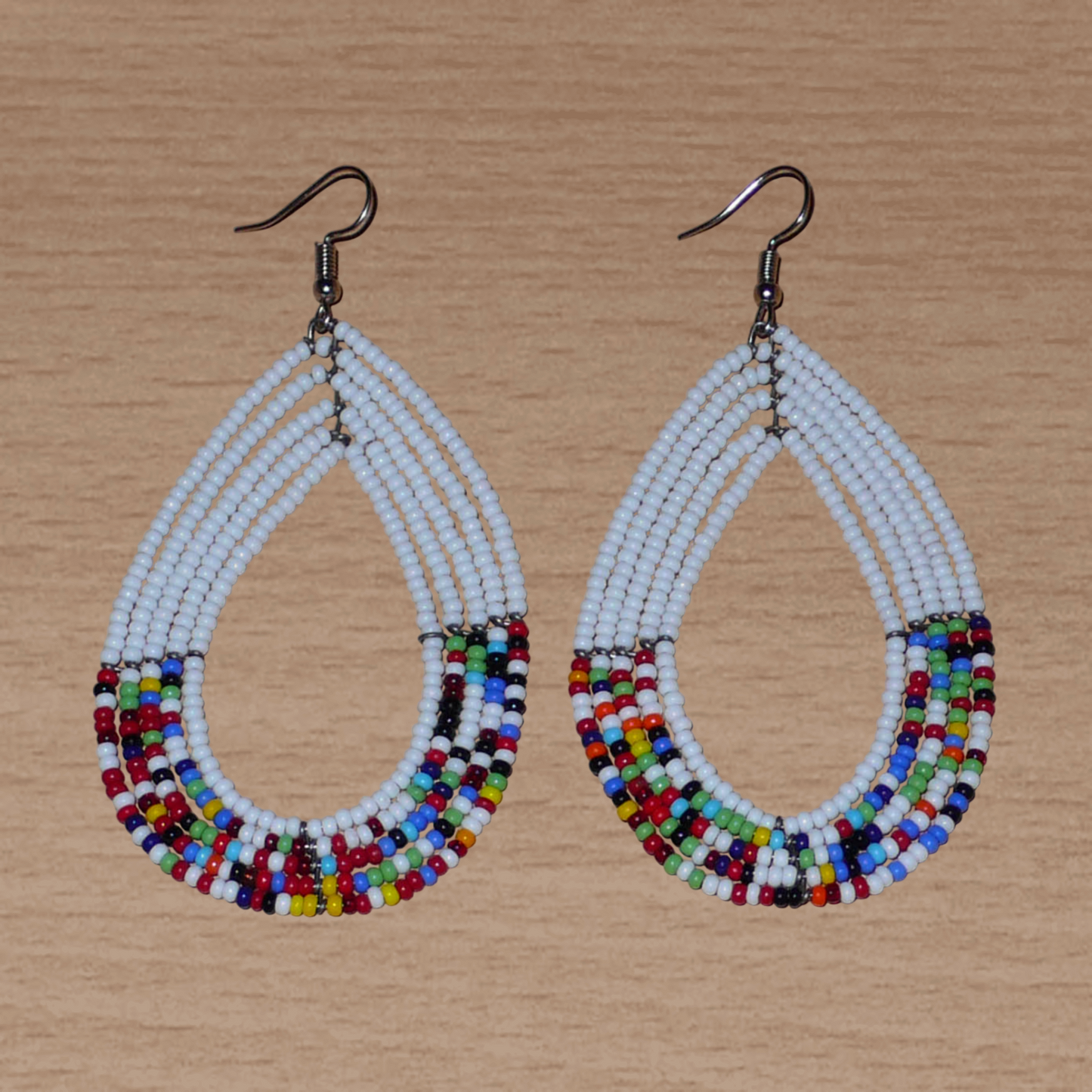 Longues boucles d'oreilles ethniques multi-rangs faites de perles de rocaille blanches et multicolores montées en forme de gouttes. Elles mesurent 9 cm de long et 4.5 cm de large, et se portent sur des oreilles percées.