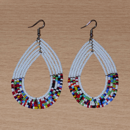 Longues boucles d'oreilles ethniques multi-rangs faites de perles de rocaille blanches et multicolores montées en forme de gouttes. Elles mesurent 9 cm de long et 4.5 cm de large, et se portent sur des oreilles percées.