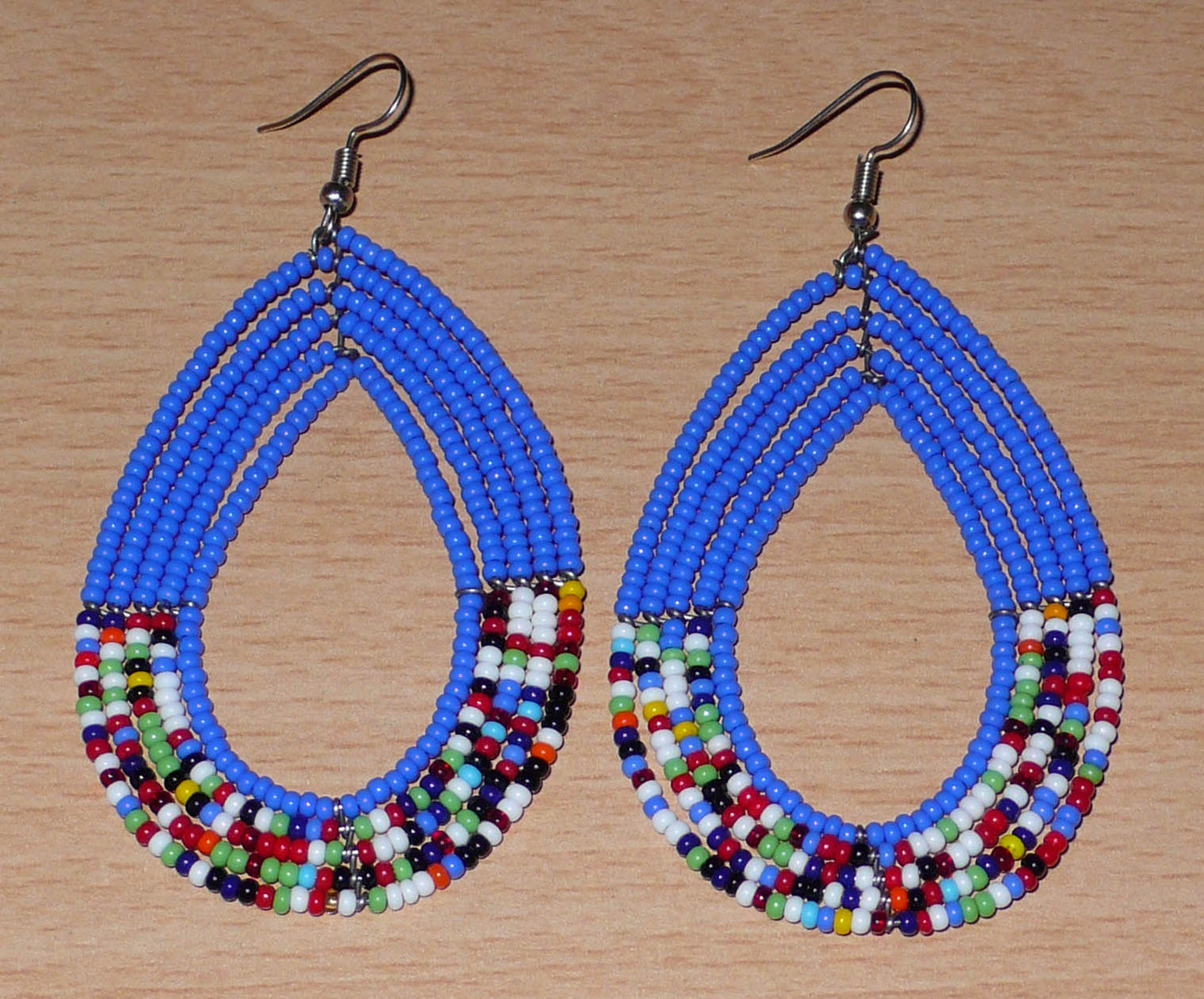 Longues boucles d'oreilles kenyanes au style afro bohème composées de perles de rocaille bleues et multicolores montées en forme de gouttes. Elles mesurent 9 cm de long et 4.5 cm de large, et se portent sur des oreilles percées.