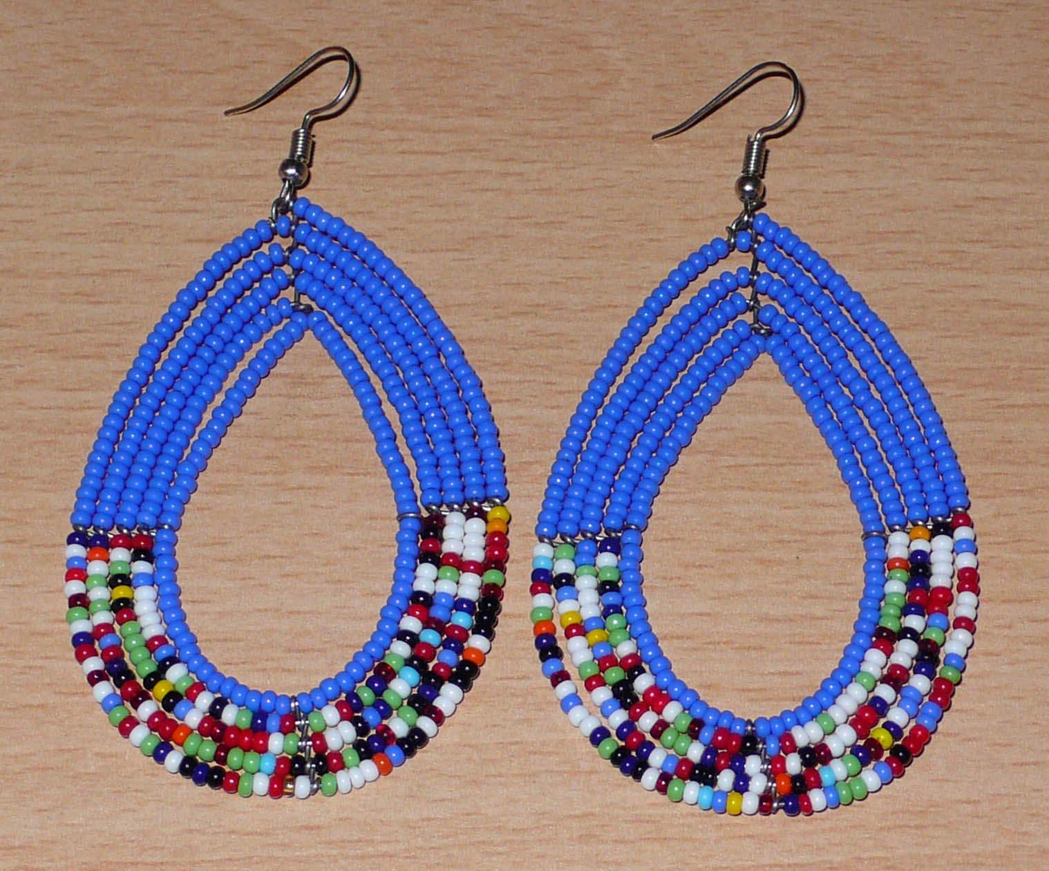 Longues boucles d'oreilles kenyanes au style afro bohème composées de perles de rocaille bleues et multicolores montées en forme de gouttes. Elles mesurent 9 cm de long et 4.5 cm de large, et se portent sur des oreilles percées.