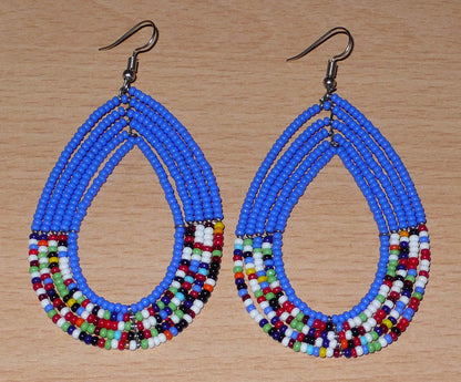 Longues boucles d'oreilles kenyanes au style afro bohème composées de perles de rocaille bleues et multicolores montées en forme de gouttes. Elles mesurent 9 cm de long et 4.5 cm de large, et se portent sur des oreilles percées.