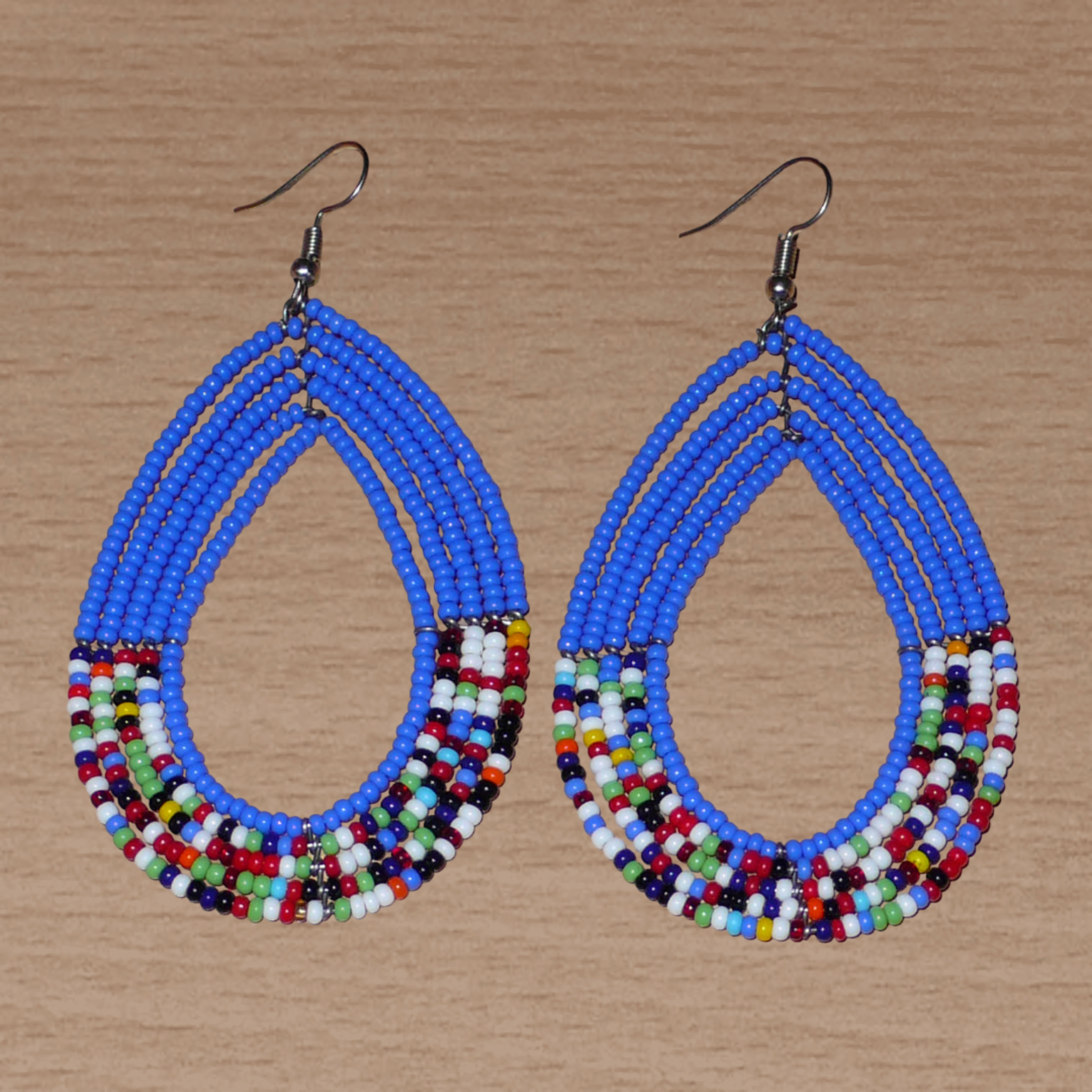 Longues boucles d'oreilles kenyanes au style afro bohème composées de perles de rocaille bleues et multicolores montées en forme de gouttes. Elles mesurent 9 cm de long et 4.5 cm de large, et se portent sur des oreilles percées.