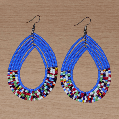 Longues boucles d'oreilles kenyanes au style afro bohème composées de perles de rocaille bleues et multicolores montées en forme de gouttes. Elles mesurent 9 cm de long et 4.5 cm de large, et se portent sur des oreilles percées.