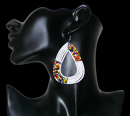 Longues et larges boucles d'oreilles kenyanes composées de perles de rocaille blanches et multicolores glissées sur cinq rangées de fils de fer montés en forme de gouttes légèrement triangulaires. Elles mesurent 8 cm de long et 5 cm de large et se portent avec des crochets en acier inoxydable sur des oreilles percées.