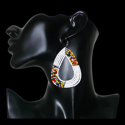 Longues et larges boucles d'oreilles kenyanes composées de perles de rocaille blanches et multicolores glissées sur cinq rangées de fils de fer montés en forme de gouttes légèrement triangulaires. Elles mesurent 8 cm de long et 5 cm de large et se portent avec des crochets en acier inoxydable sur des oreilles percées.