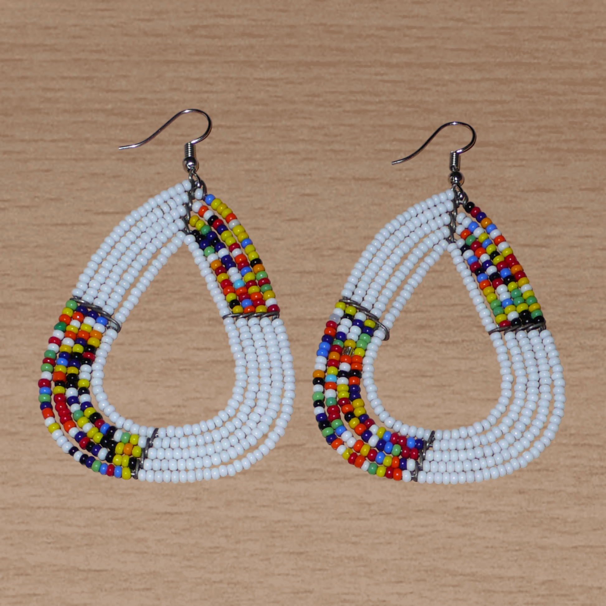 Longues et larges boucles d'oreilles kenyanes composées de perles de rocaille blanches et multicolores glissées sur cinq rangées de fils de fer montés en forme de gouttes légèrement triangulaires. Elles mesurent 8 cm de long et 5 cm de large et se portent avec des crochets en acier inoxydable sur des oreilles percées.