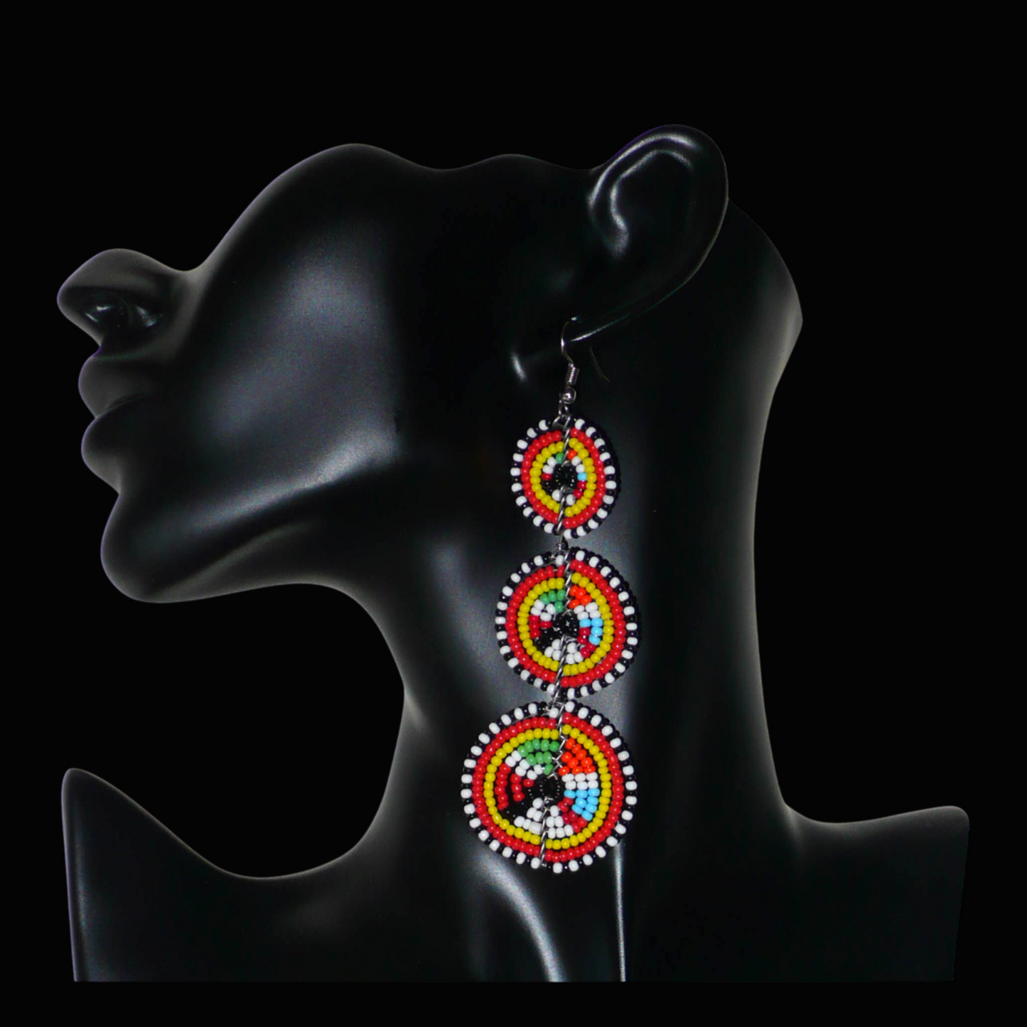 Longues boucles d'oreilles africaines de tradition Massai aux design et couleurs évoquant le style ethnique afro chic des années 70. Elles se composent de perles de rocaille multicolores glissées sur des fils de fer montés en forme de trois cercles superposés. Ces boucles d'oreilles mesurent 10.5 cm de long et 3 cm de large ; elles se portent avec des crochets en acier inoxydable sur des oreilles percées.