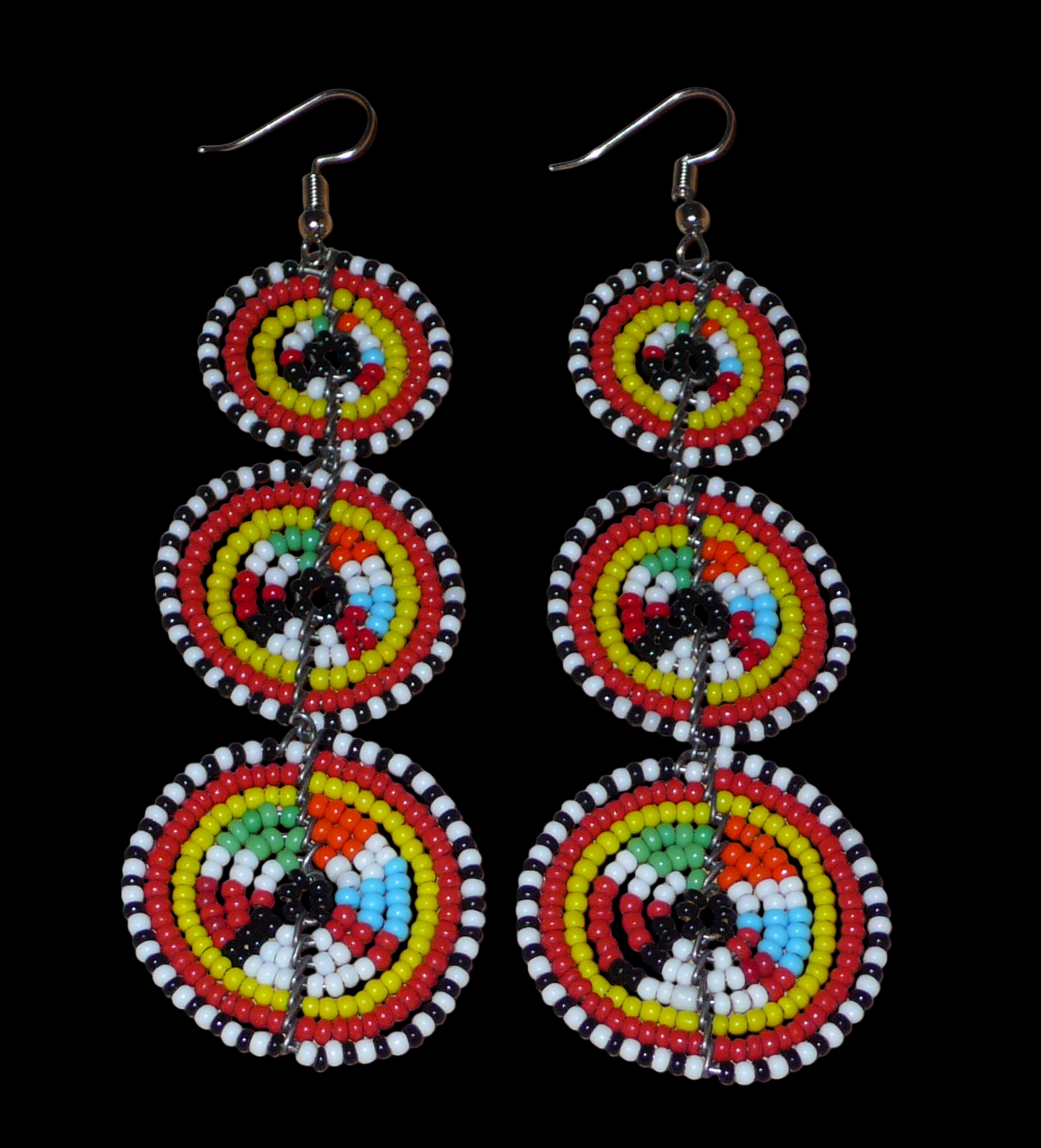 Longues boucles d'oreilles africaines de tradition Massai aux design et couleurs évoquant le style ethnique afro chic des années 70. Elles se composent de perles de rocaille multicolores glissées sur des fils de fer montés en forme de trois cercles superposés. Ces boucles d'oreilles mesurent 10.5 cm de long et 3 cm de large ; elles se portent avec des crochets en acier inoxydable sur des oreilles percées.