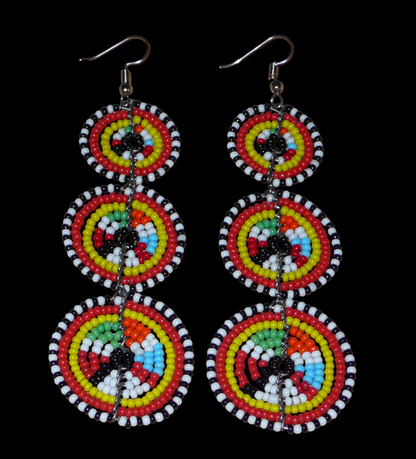 Longues boucles d'oreilles africaines de tradition Massai aux design et couleurs évoquant le style ethnique afro chic des années 70. Elles se composent de perles de rocaille multicolores glissées sur des fils de fer montés en forme de trois cercles superposés. Ces boucles d'oreilles mesurent 10.5 cm de long et 3 cm de large ; elles se portent avec des crochets en acier inoxydable sur des oreilles percées.