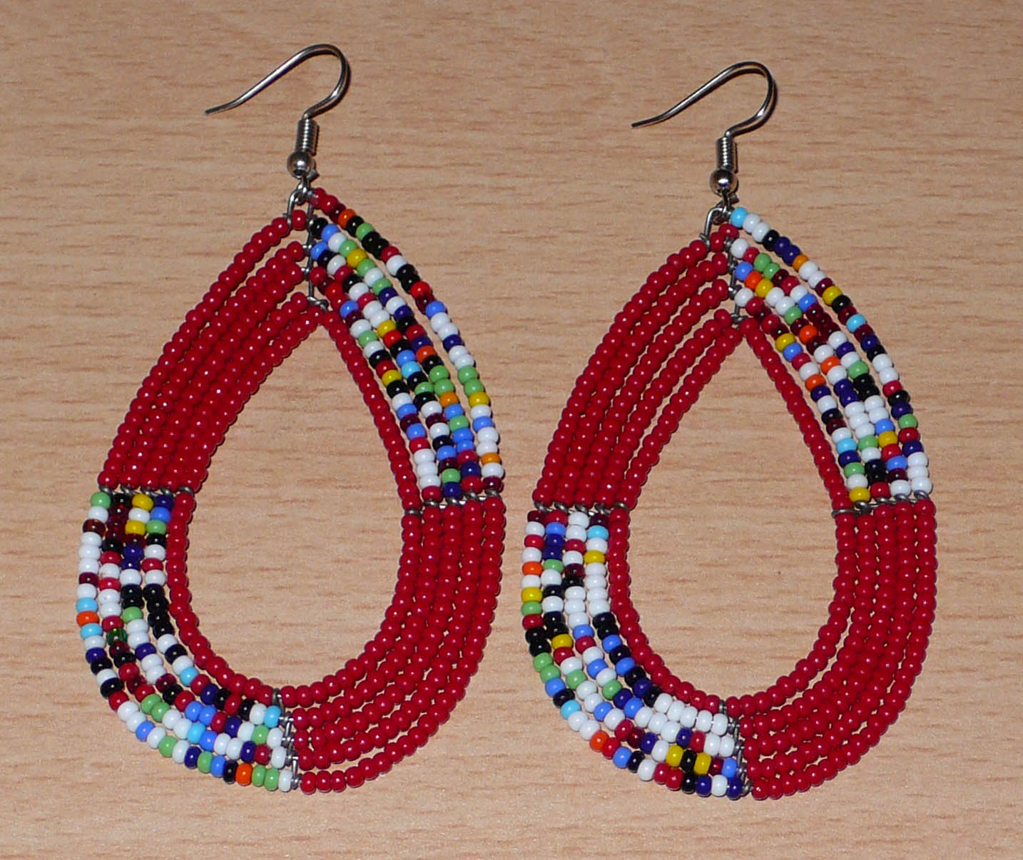 Longues boucles d'oreilles Massai multi-rangs rouges et multicolores en perles de rocaille. Elles mesurent 9 cm de long et 4.5 cm de large et se portent sur des oreilles percées.