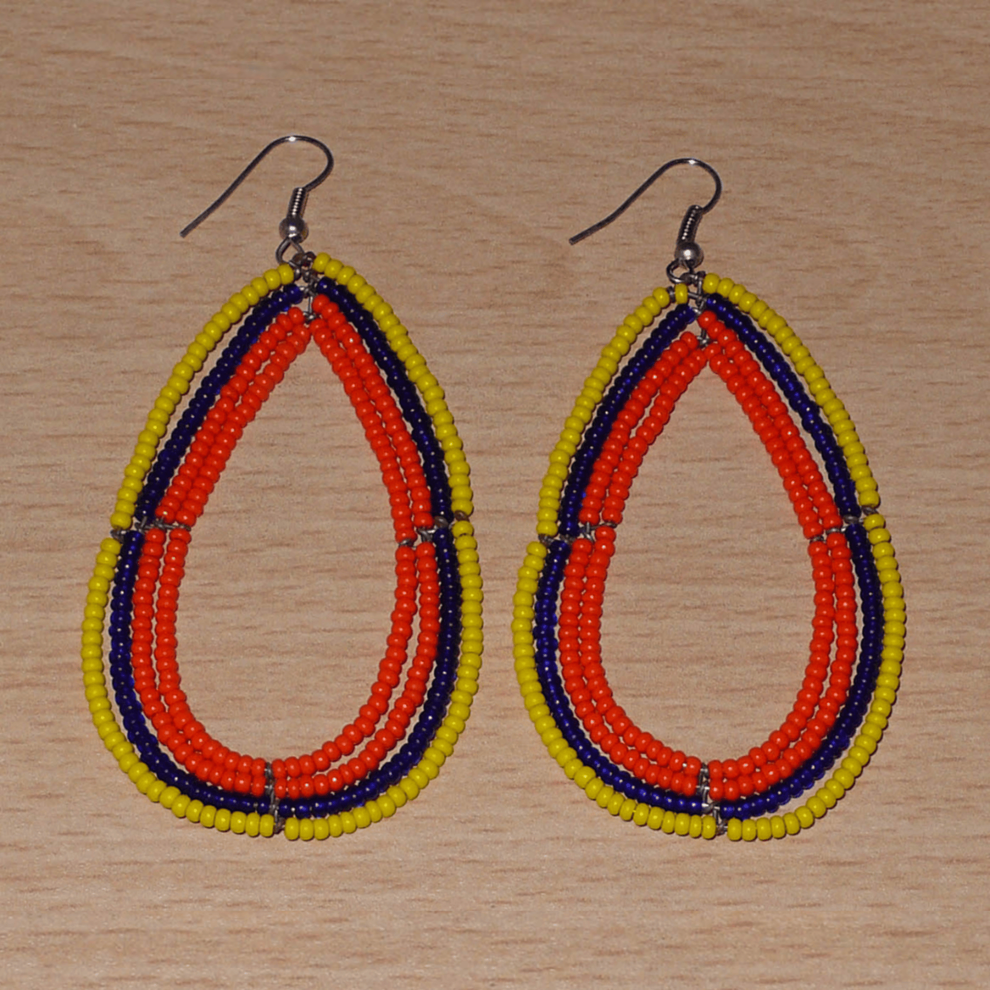 Longues boucles d'oreilles tricolores composées de perles de rocaille orange, jaunes et bleu marine enfilées sur quatre rangées de fils de fer montés en forme de gouttes. Ces boucles d'oreilles "oversized" mesurent 8.5 cm de long et 4.5 cm de large ; elles se portent avec des crochets en acier inoxydable sur des oreilles percées.