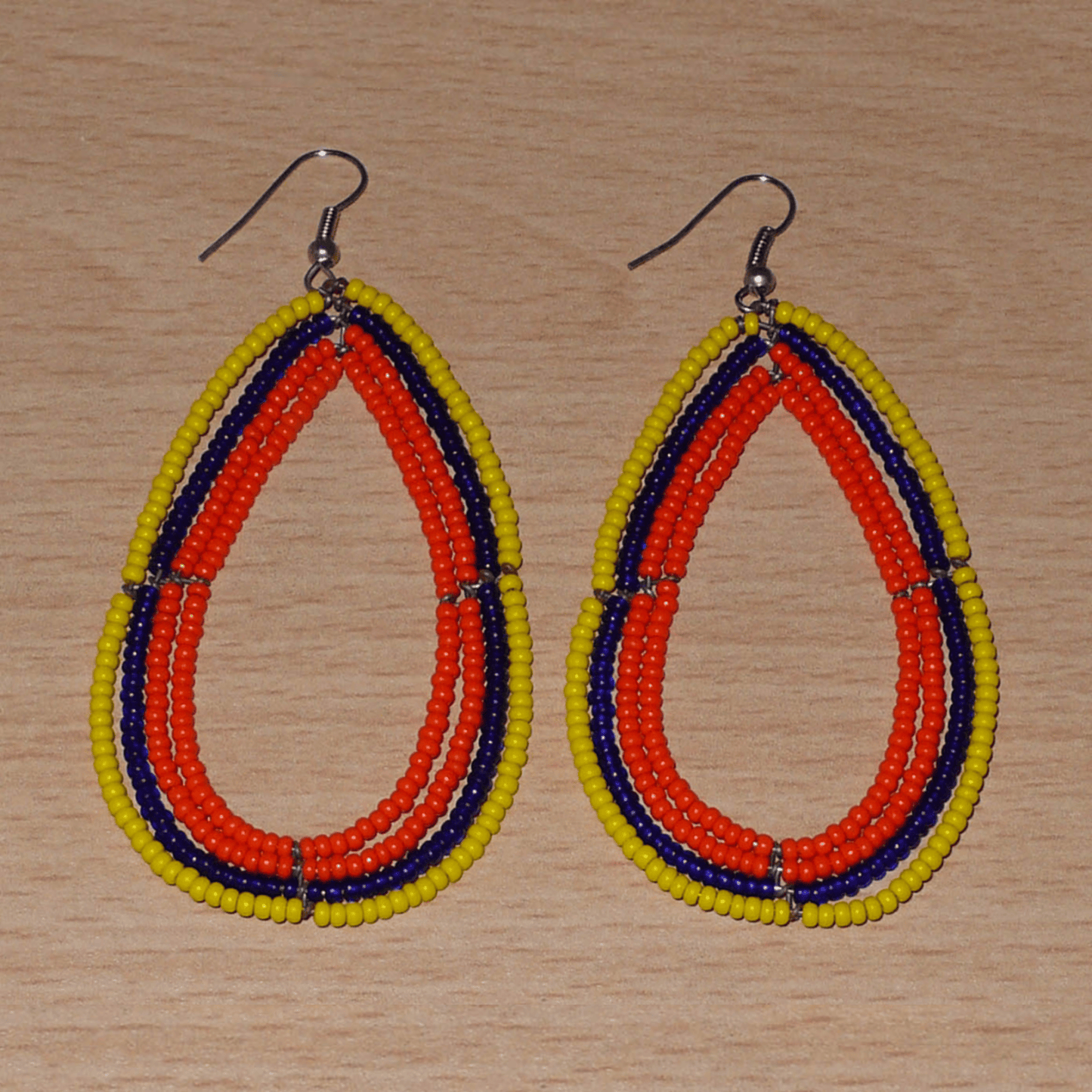 Longues et larges boucles d'oreilles ethniques multi-rangs en perles de rocaille orange, jaunes et bleu marine. Elles mesurent 8.5 cm de long et 4.5 cm de large, et se portent sur des oreilles percées.