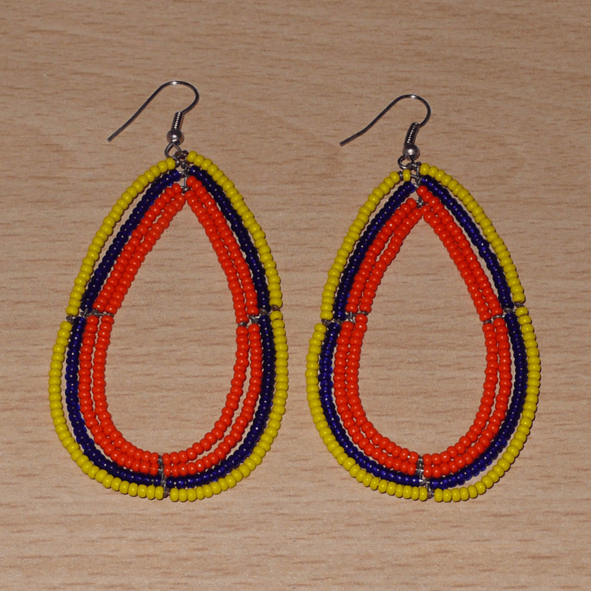 Longues et larges boucles d'oreilles ethniques multi-rangs en perles de rocaille orange, jaunes et bleu marine. Elles mesurent 8.5 cm de long et 4.5 cm de large, et se portent sur des oreilles percées.