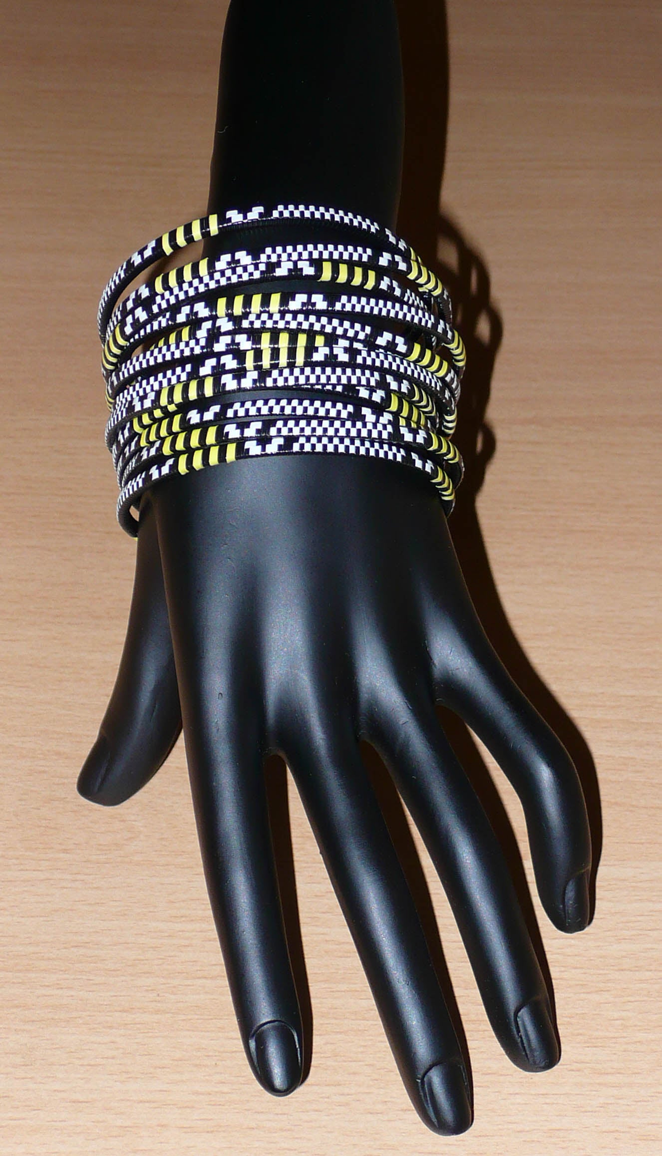 Lot de douze bracelets africains tricolores fins et légers à porter, composés de fines bandes de plastique recyclé jaune, noir et blanc.