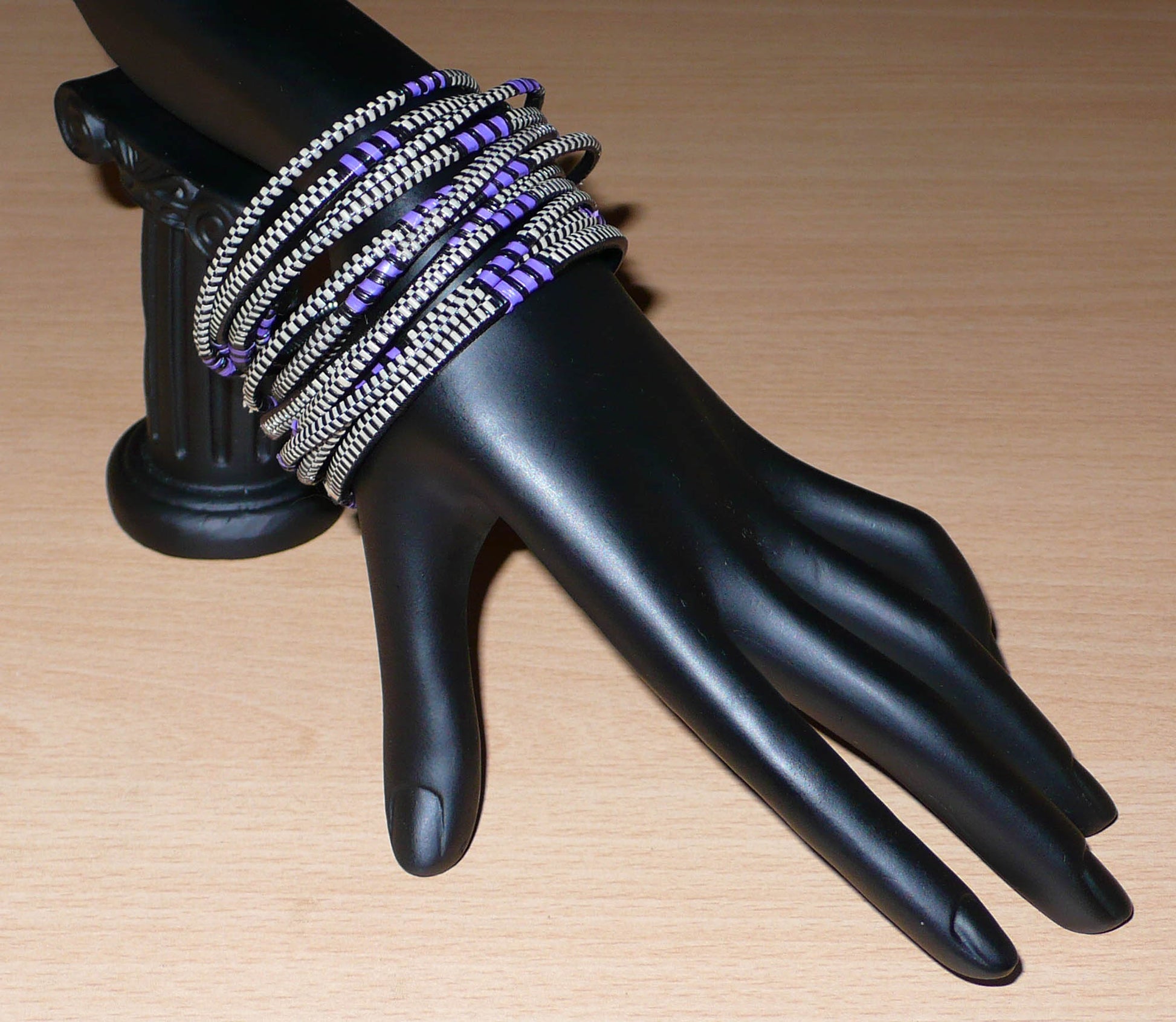 Ensemble de 12 bracelets africains tricolores fabriqués au Mali dans une approche éco-responsable : très fins, ils sont composés de fines bandes de plastique recyclé violet, noir et blanc. Ces bracelets, à empiler sur vos poignets, ont une circonférence de 19.5 cm, un diamètre de 6.3 cm et une épaisseur de 0.4 cm.
