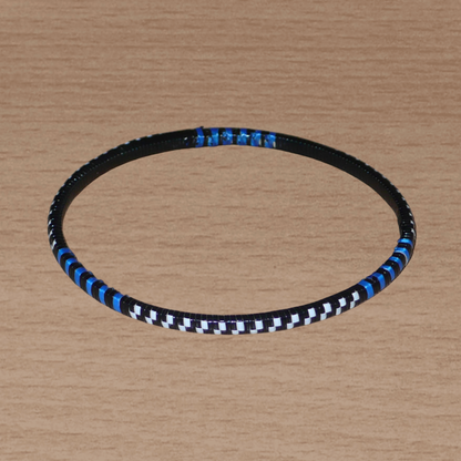 Lot de douze bracelets africains tricolores bleus, blancs et noirs, faits de lamelles en carton recouvertes d'un tissage de fines bandes de plastique recyclé.