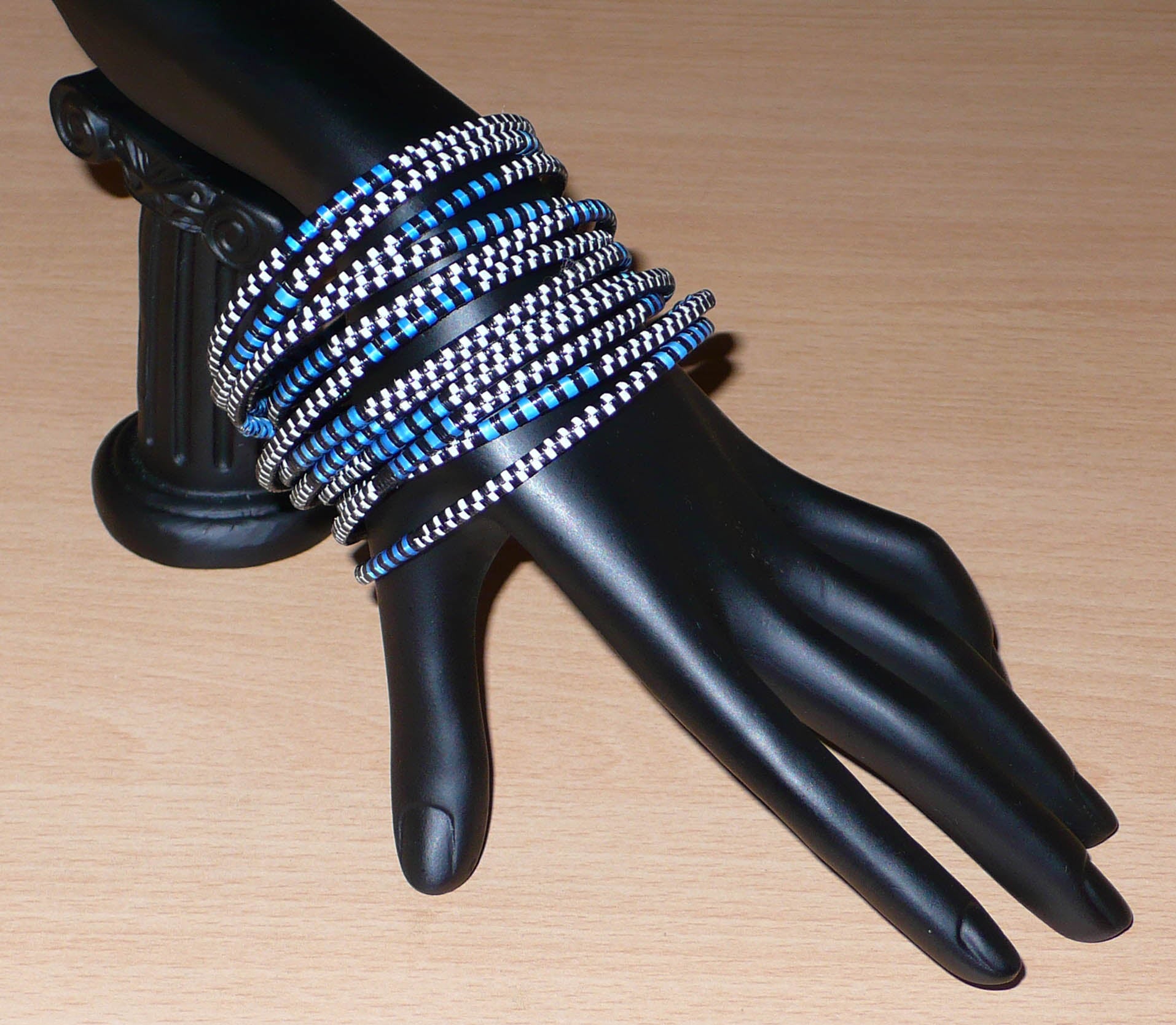 Lot de douze bracelets africains tricolores bleus, blancs et noirs, faits de lamelles en carton recouvertes d'un tissage de fines bandes de plastique recyclé.