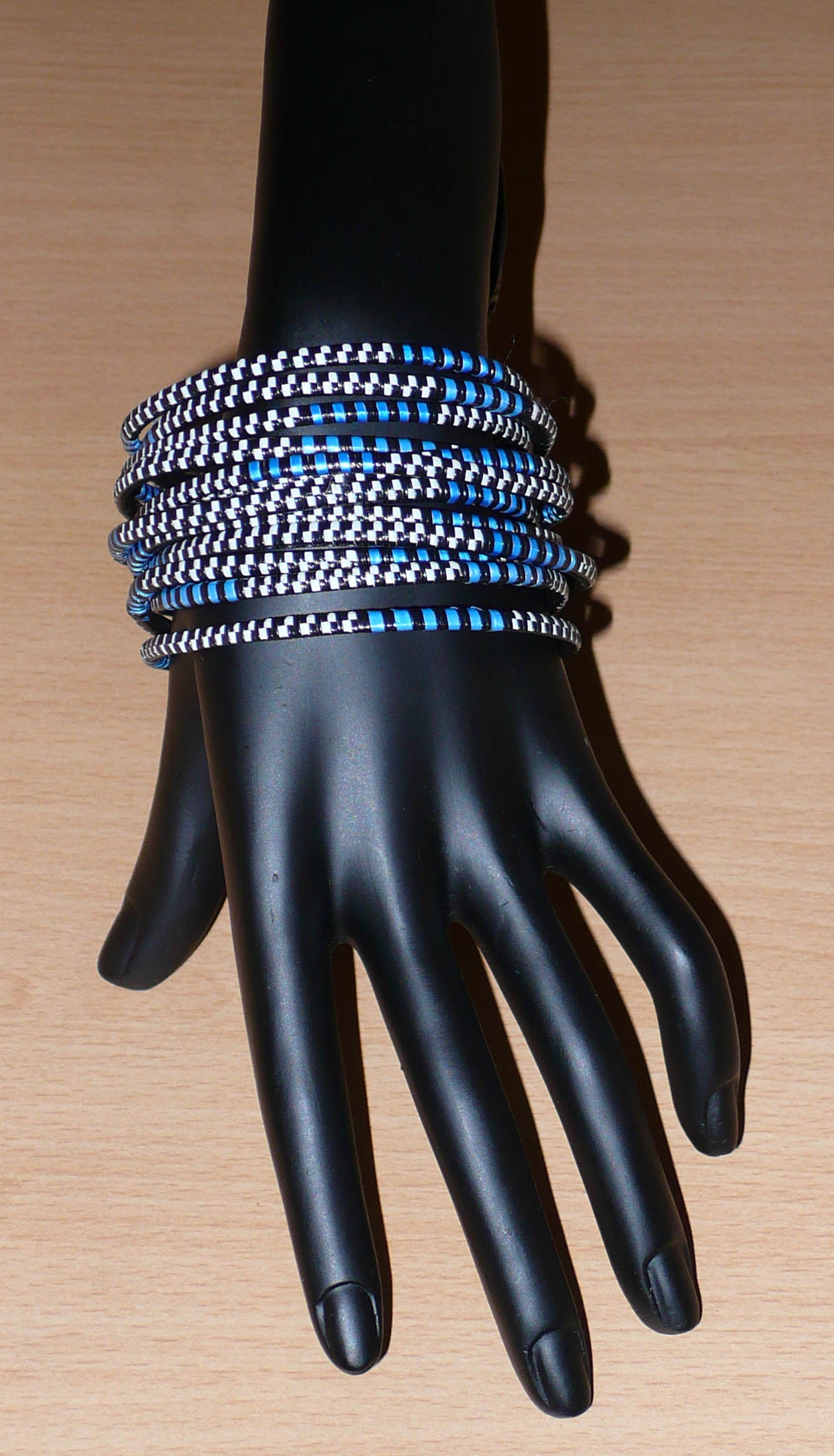 Lot de douze bracelets africains tricolores bleus, blancs et noirs, faits de lamelles en carton recouvertes d'un tissage de fines bandes de plastique recyclé.