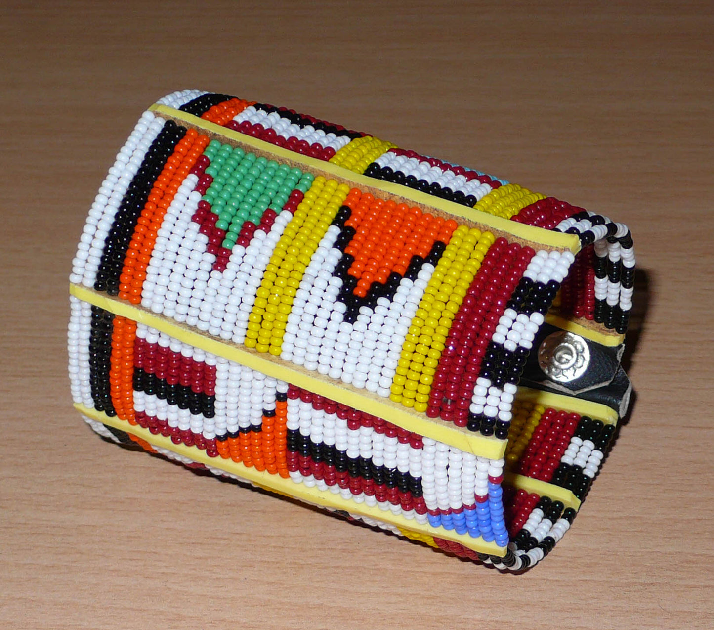 Manchette africaine multi-rangs à motifs ethniques traditionnels Massai composée de trente-six rangées de perles de rocaille multicolores glissées sur des fils de fer fixés sur des charnières en plastique jaune.