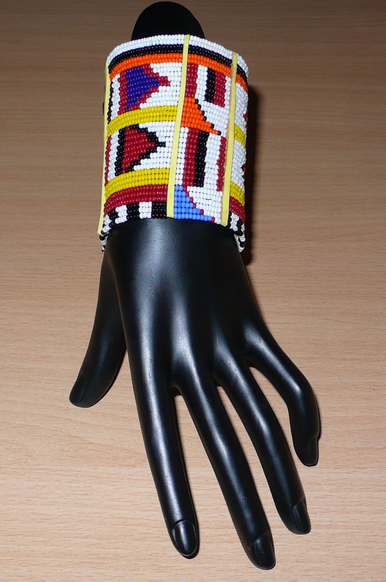 Manchette africaine multi-rangs à motifs ethniques traditionnels Massai composée de trente-six rangées de perles de rocaille multicolores glissées sur des fils de fer fixés sur des charnières en plastique jaune.