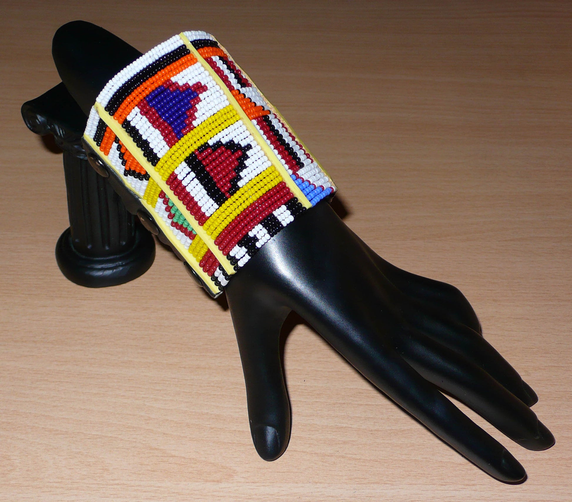 Manchette africaine multi-rangs à motifs ethniques traditionnels Massai composée de trente-six rangées de perles de rocaille multicolores glissées sur des fils de fer fixés sur des charnières en plastique jaune.