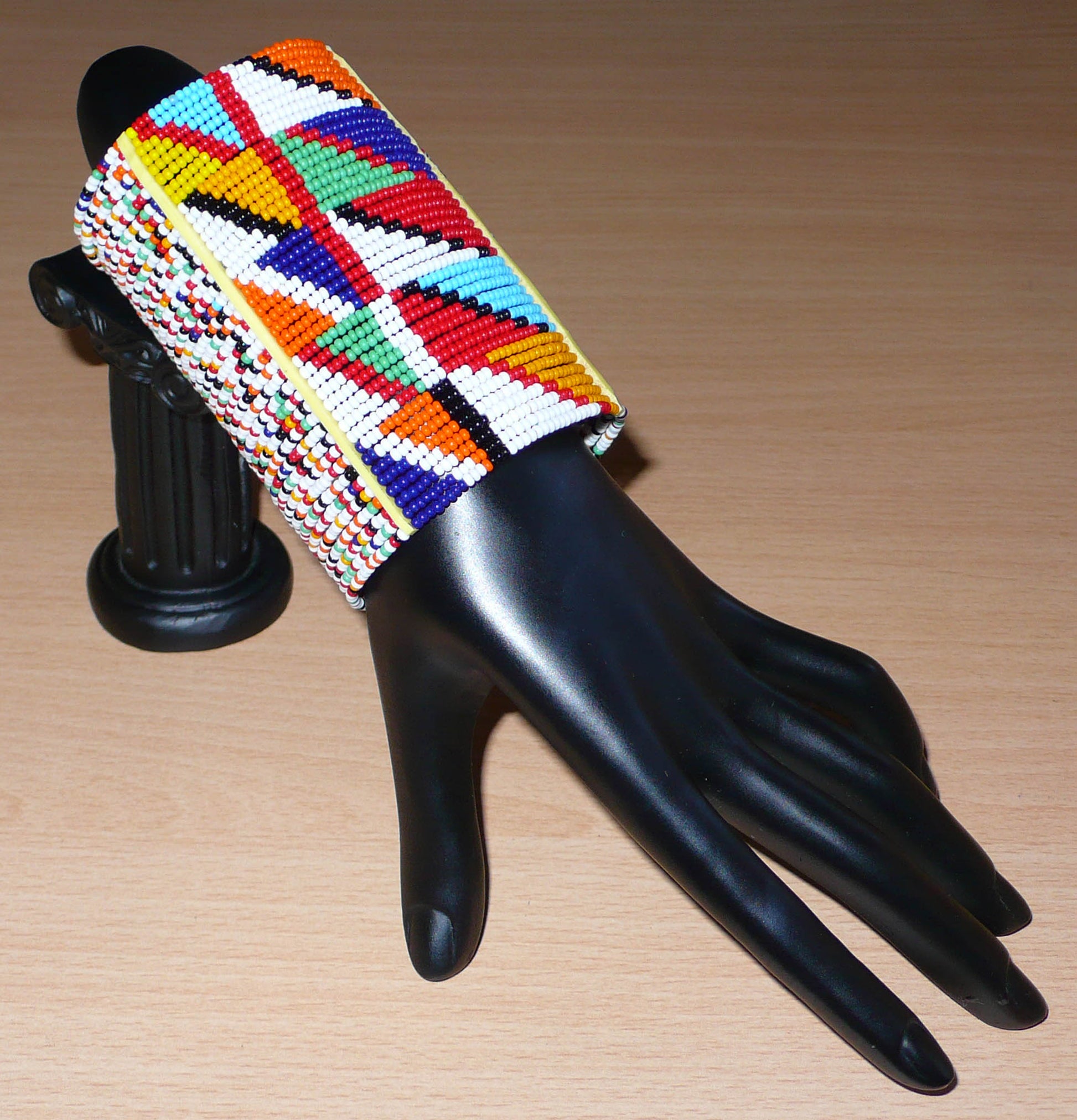 Manchette haute multi-rangs à motifs géométriques ethniques Massai composée de perles de rocaille multicolores ; elle s'attache avec trois boutons pressions.