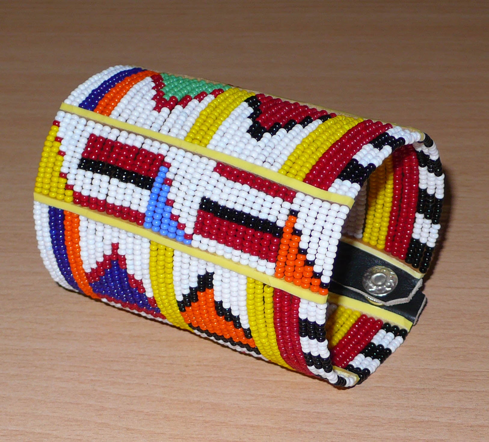 Manchette africaine perlée à motifs ethniques Massai composée de plusieurs rangs de perles de rocaille multicolores glissées sur des fils de fer fixés sur des charnières en plastique.