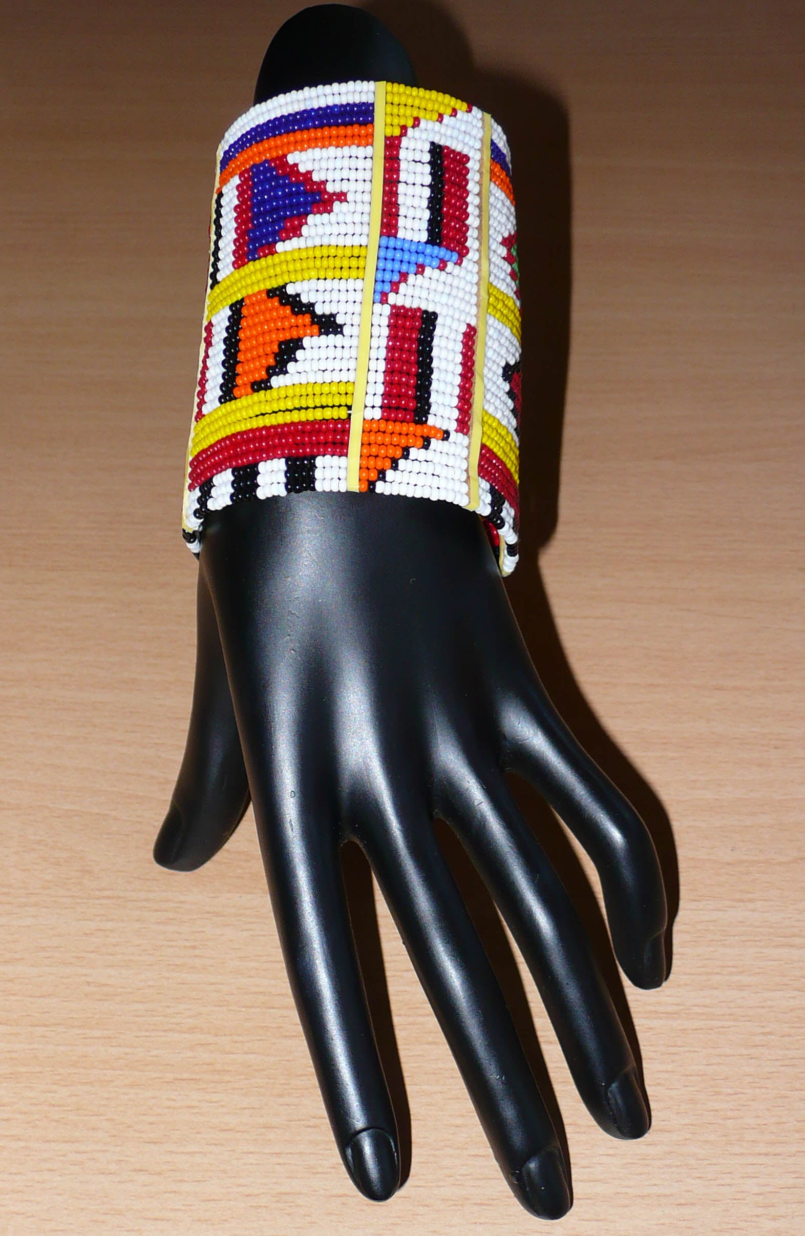 Manchette africaine perlée à motifs ethniques Massai composée de plusieurs rangs de perles de rocaille multicolores glissées sur des fils de fer fixés sur des charnières en plastique.