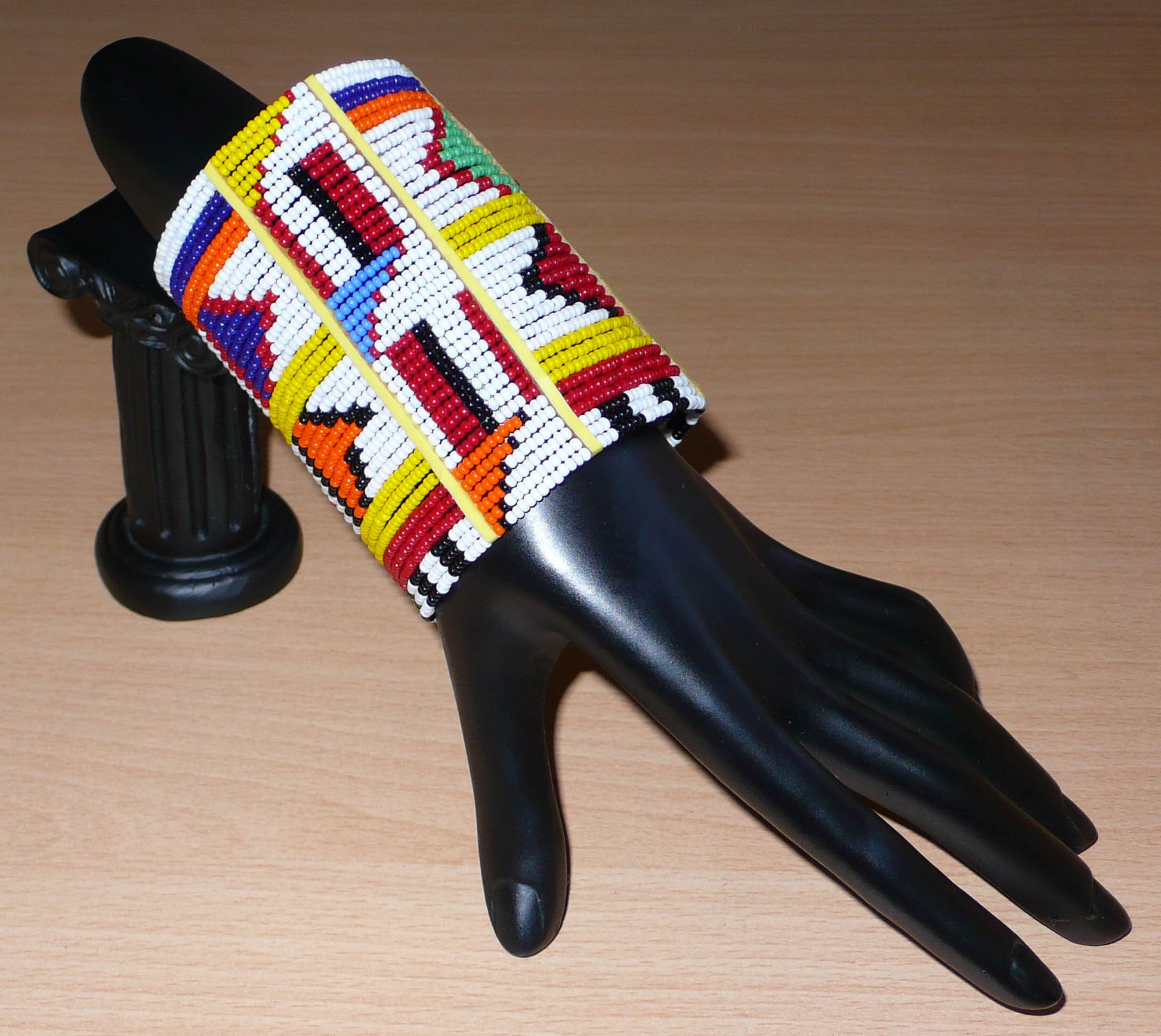 Manchette africaine perlée à motifs ethniques Massai composée de plusieurs rangs de perles de rocaille multicolores glissées sur des fils de fer fixés sur des charnières en plastique.