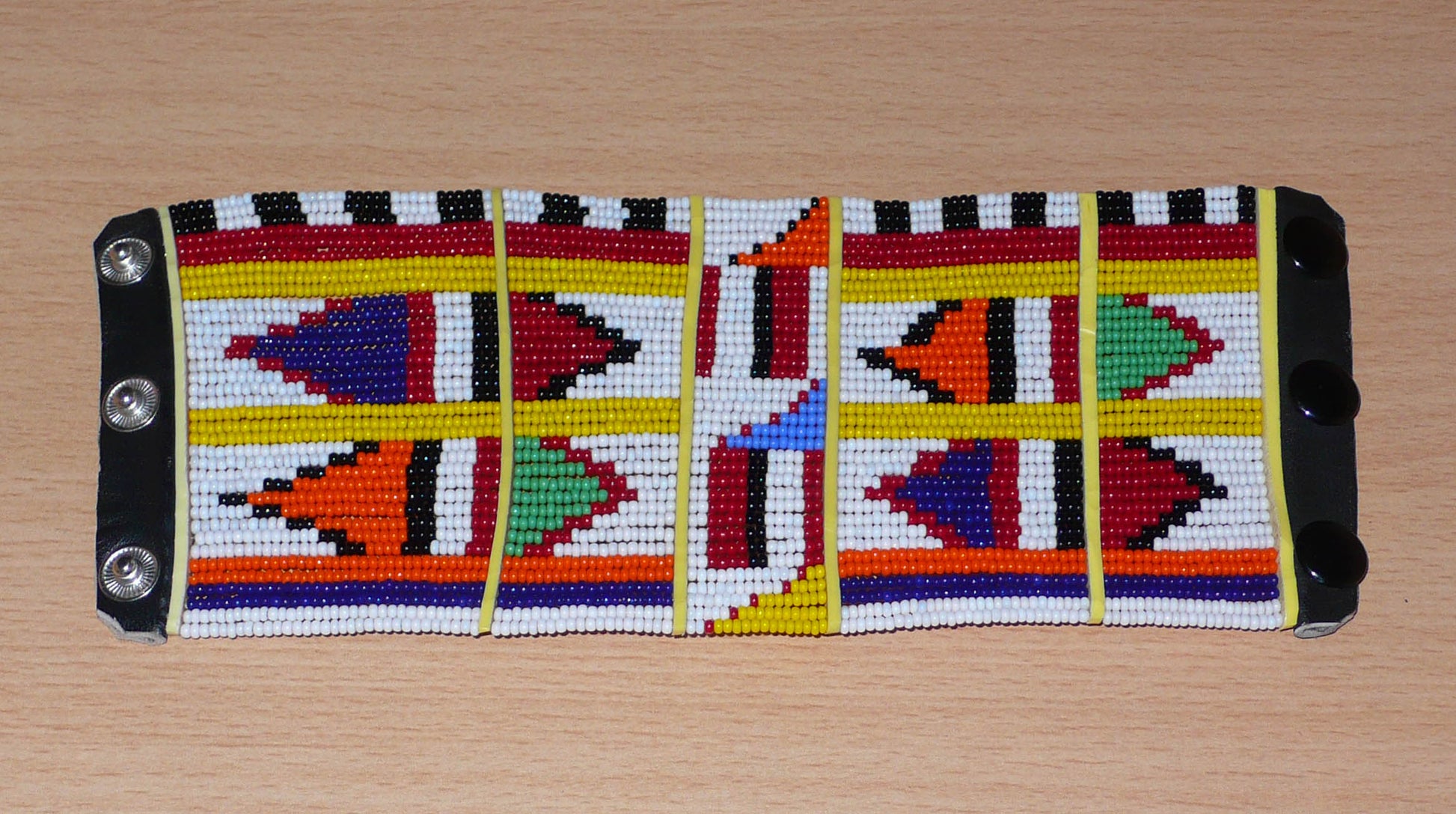 Manchette africaine perlée à motifs ethniques Massai composée de plusieurs rangs de perles de rocaille multicolores glissées sur des fils de fer fixés sur des charnières en plastique.