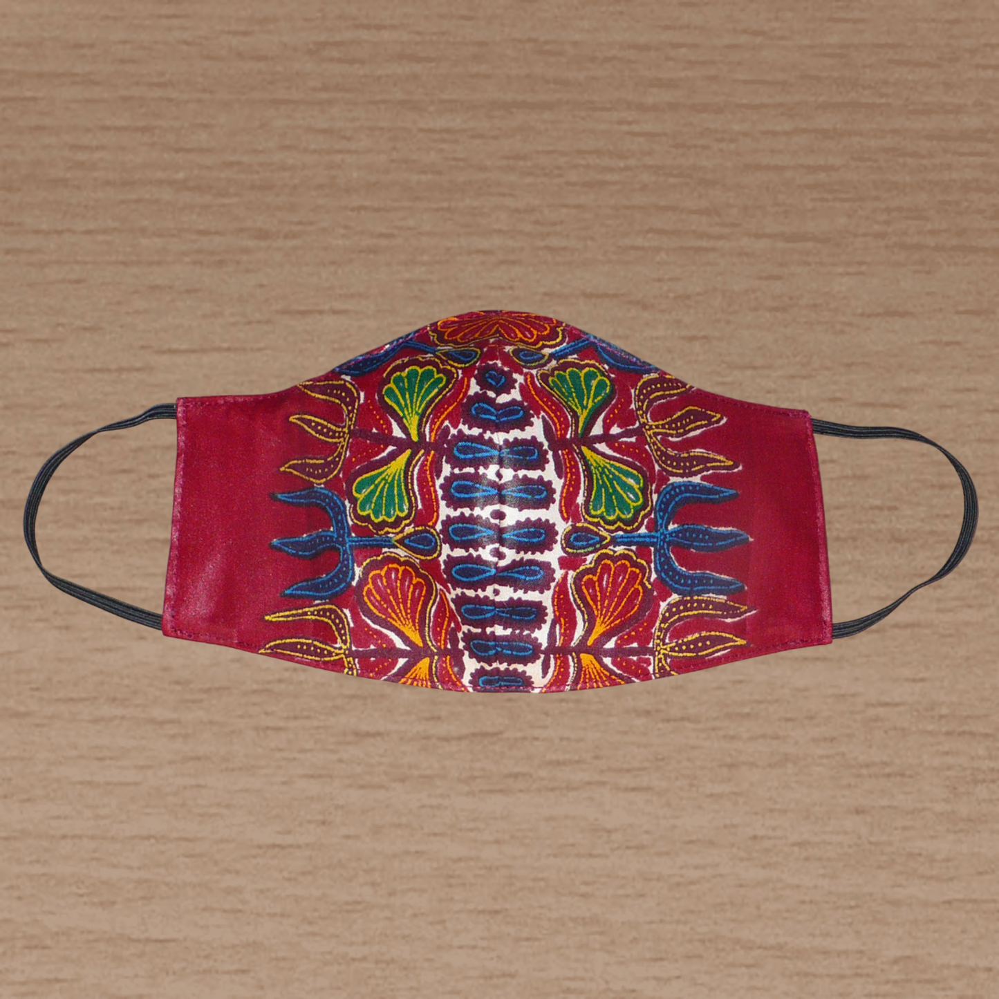 Masque facial en tissu africain bordeaux imprimé de motifs floraux à porter avec des élastiques. En vue d'une utilisation eco-responsable, il est lavable et réutilisable.