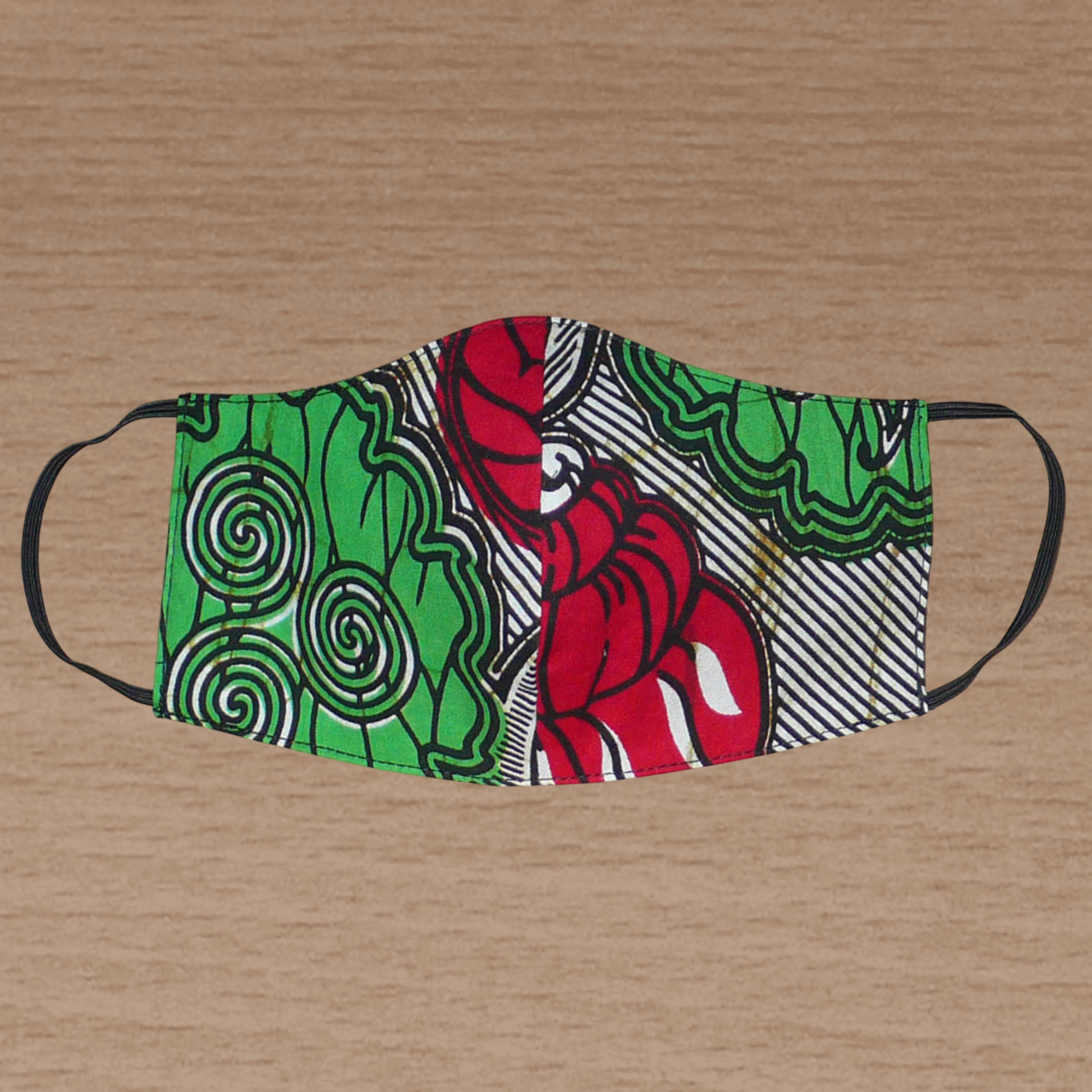Masque facial en tissu africain en coton imprimé de motifs verts, rouges, noirs et blancs ; il se porte avec des élastiques. En vue d'une utilisation éco-responsable, ce masque est lavable et réutilisable.