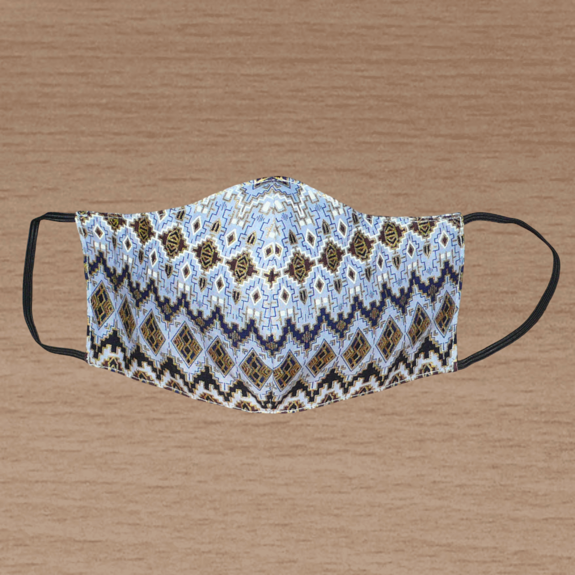 Masque facial textile à la coupe ajustée, cousu dans un tissu en coton bleu ciel à motifs ethniques bleu marine, blancs, marron et dorés ; il se porte avec des élastiques.