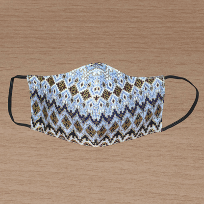Masque facial textile à la coupe ajustée, cousu dans un tissu en coton bleu ciel à motifs ethniques bleu marine, blancs, marron et dorés ; il se porte avec des élastiques.
