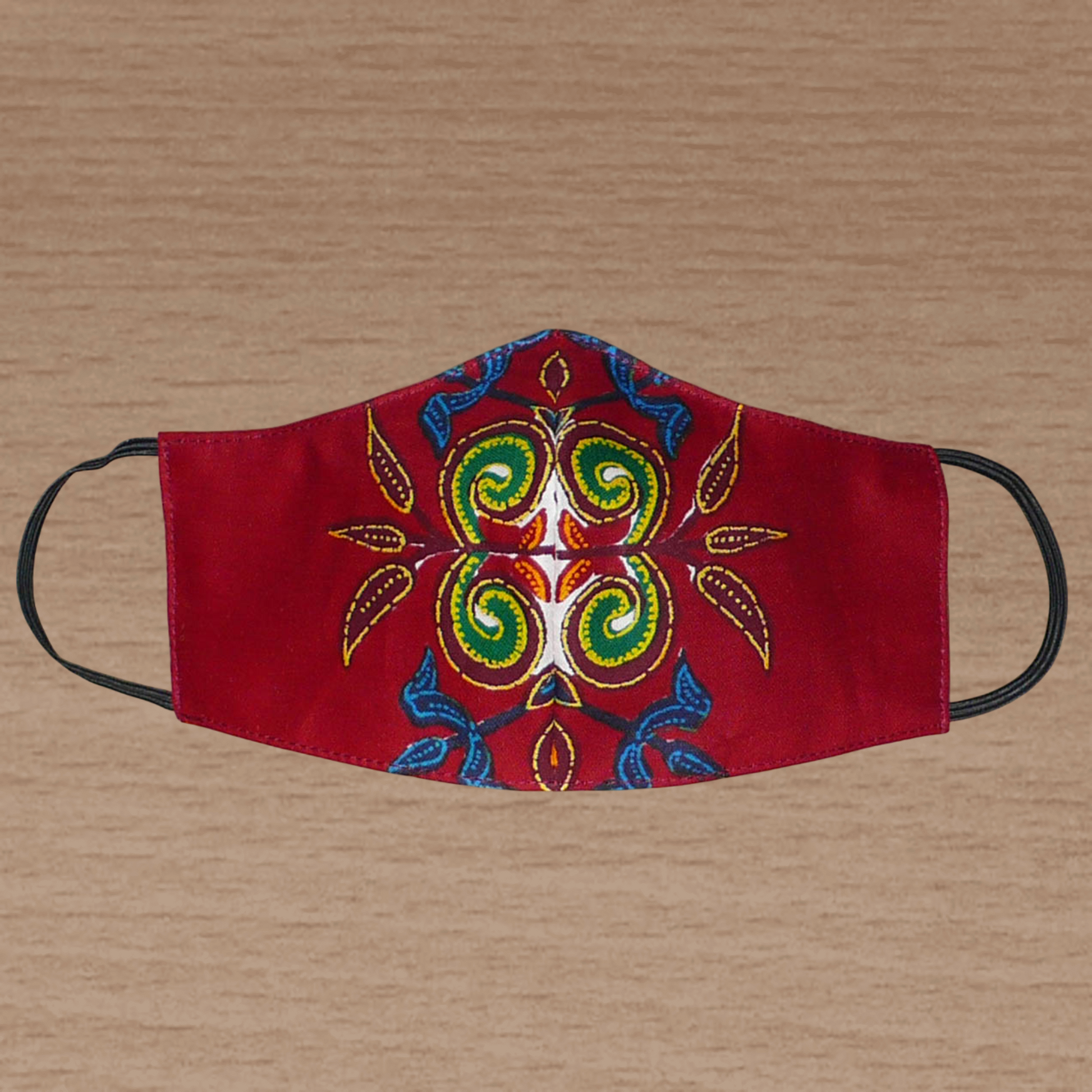 Masque en tissu africain bordeaux imprimé de motifs exotiques multicolores ; il se porte avec des élastiques. En vue d'un usage éco-responsable, il est lavable et réutilisable.