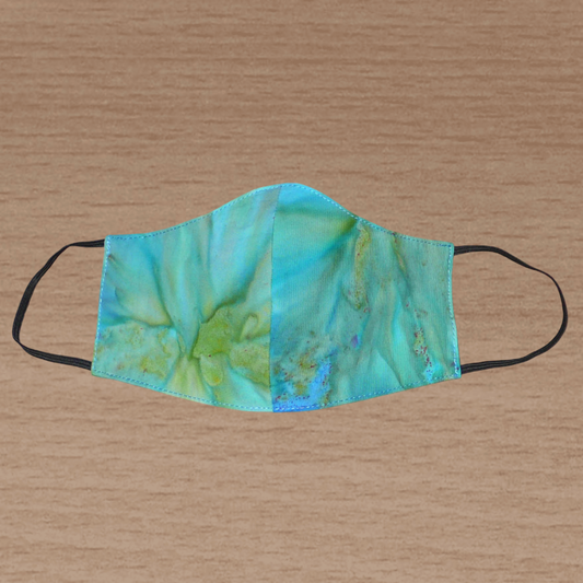 Masque facial textile en coton imprimé Tie and Dye bleu turquoise, avec des nuances de jaune et de vert ; à porter avec des élastiques.