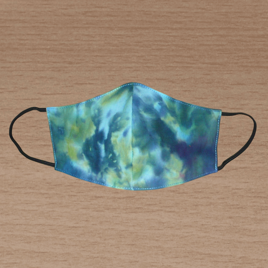 Masque facial coupé et cousu dans un tissu en coton imprimé Tie and Dye bleu avec des nuances de jaune et de rose ; il se porte avec des élastiques. Conçu dans l'optique d'une utilisation eco-friendly, ce masque est lavable et réutilisable.