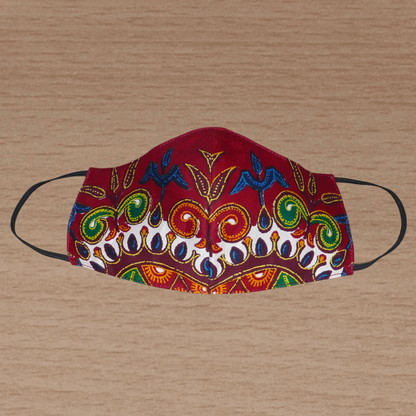 Masque facial textile à la coupe ajustée, cousu dans un tissu en coton bordeaux imprimé de motifs exotiques floraux multicolores.