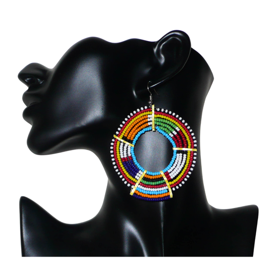 Bijou artisanal fabriqué au Kenya, cette mono boucle africaine Massai, à porter sur une seule oreille pour créer une asymétrie visuelle, apportera de la couleur à votre look ! Elle se compose de perles de rocaille multicolores glissées sur des fils de fer montés en cercles fixés sur des charnières en plastique recyclé jaune. Surdimensionnée, cette longue et large mono boucle mesure 8.5 cm de long.