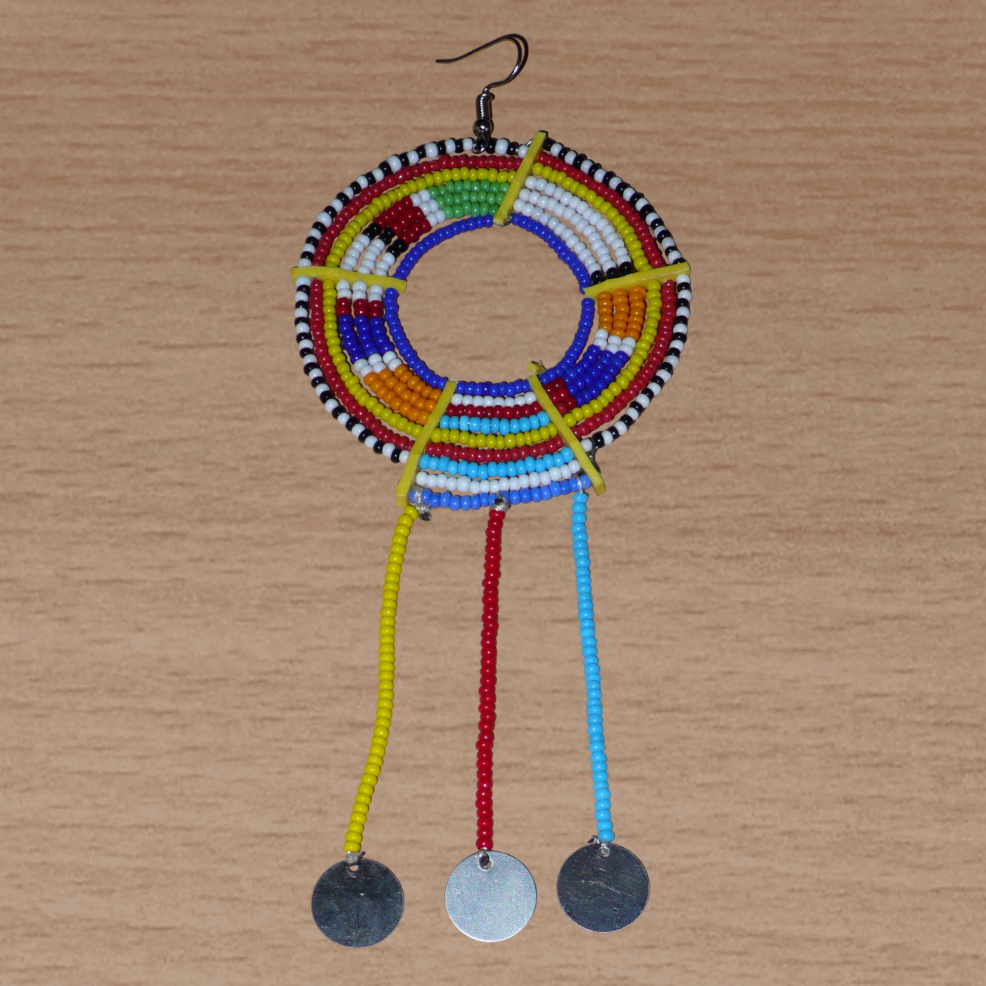 Mono boucle d'oreille africaine Massai à porter sur une seule oreille pour créer un effet d'asymétrie visuelle : elle se compose de perles de rocaille bleues et multicolores enfilées sur des fils de fer montés en cercles fixés sur des charnières en plastique recyclé jaune ; il se prolonge de franges perlées ornées de disques en métal. Surdimensionnée, cette mono boucle d'oreille à l'allure exotique mesure 15 cm de long.