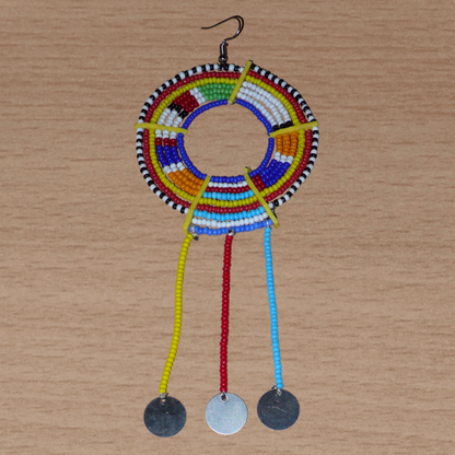 Mono boucle d'oreille africaine Massai à porter sur une seule oreille pour créer un effet d'asymétrie visuelle : elle se compose de perles de rocaille bleues et multicolores enfilées sur des fils de fer montés en cercles fixés sur des charnières en plastique recyclé jaune ; il se prolonge de franges perlées ornées de disques en métal. Surdimensionnée, cette mono boucle d'oreille à l'allure exotique mesure 15 cm de long.